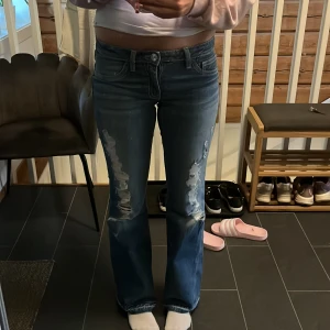 Blå bootcut jeans Gina Tricot 170 - Snygga blå bootcut jeans från Gina Tricot i storlek 170. Jeansen har slitna detaljer framtill, klassisk femficksmodell och låg midja. Materialet är jeans med en skön känsla och bakfickor med dekorativa sömmar.