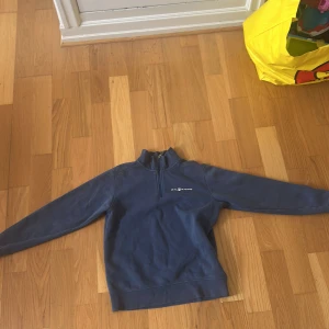 Blå half zip tröja från Sail Racing - Mörkblå långärmad tröja från Sail Racing med half zip och hög krage. Tröjan har en stilren logga på bröstet och en liten detalj i nacken. Perfekt för dig som gillar sportig och clean stil.