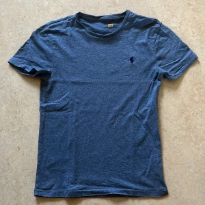 Blå t-shirt från Ralph Lauren - Snygg blå t-shirt från Ralph Lauren med klassisk broderad logga på bröstet. T-shirten har rund halsringning och korta ärmar. Tillverkad i mjuk bomull som känns skön mot huden. 