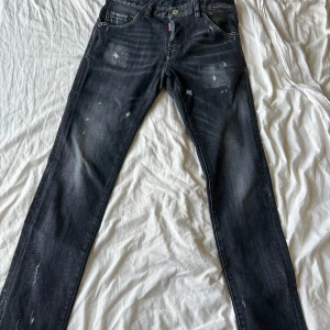 Svarta Dsquared2 jeans med slitningar - Snygga svarta jeans från Dsquared2 med diskreta slitningar och tvättade detaljer. Klassisk femficksmodell med rakt snitt och normal passform. Storlek 12Y, Jeansen har Dsquared2-logga på myntfickan och bakfickan. Perfekta för dig som gillar streetstyle. 