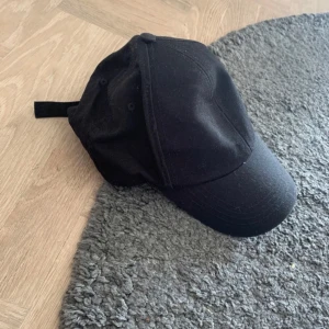 Svart keps från H&M M/L - En stilren svart keps från H&M i storlek M/L. Klassisk böjd skärm och justerbar rem baktill för perfekt passform. Tillverkad i mjukt bomullsmaterial som andas. Perfekt accessoar för en avslappnad och cool look.