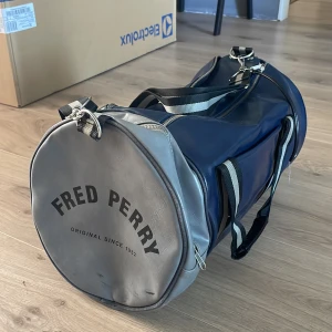 Fred Perry marinblå träningsväska - Fred Perry väska | skick 4/10 den här ett par defekter och dragkedjan på ena sidan har åkt av. Nypris runt 1600kr mitt pris 200.