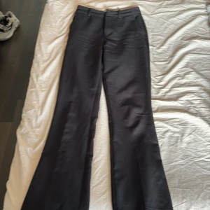 Svarta kostymbyxor från Bik Bok - Svarta kostymbyxor från Bik Bok i klassisk modell med raka ben och hällor för bälte. Byxorna har diskreta fickor bak och stängs med dragkedja och hake. Snygg passform och stilren look, perfekta till en dressad outfit.