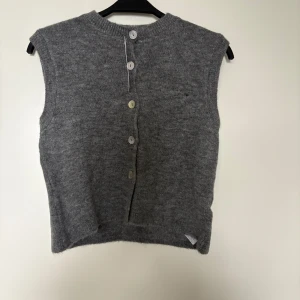 Grå stickad väst från Gina Tricot - Mysig gråmelerad stickad väst från Gina Tricot i loose fit. Västen har rund halsringning och knappar som en snygg detalj. Perfekt att slänga över en skjorta eller t-shirt för en chill look. Med prislappen kvar.
