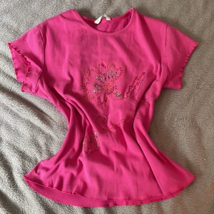 Rosa T-shirt med broderad blomma Marks & Spencer - Superfin rosa t-shirt från Marks & Spencer med broderad blomma och paljettdetaljer framtill. Mjuk och skön i bomull, kortärmad och med lätt utställd passform. Perfekt för dig som vill sticka ut med färg och detaljer!