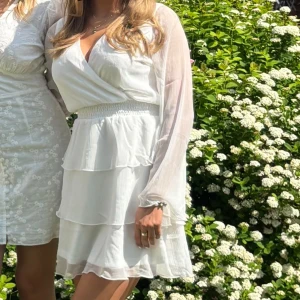 Vit omlottklänning med volanger - Superfin vit kortklänning med omlottliv, v-ringning och långa transparenta ärmar. Perfekt för sommarens alla tillfällen! Materialet känns lätt och luftigt. Köpt från bubbleroom för 699kr