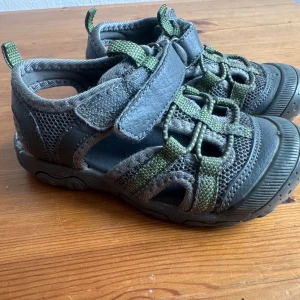 Barn Sandaler Grå Strl 24 - Ett par grå barn sandaler . Perfekt för varma dagar och lek utomhus. Sandalerna har en praktisk kardborreknäppning som gör det enkelt att ta på och av dem. 