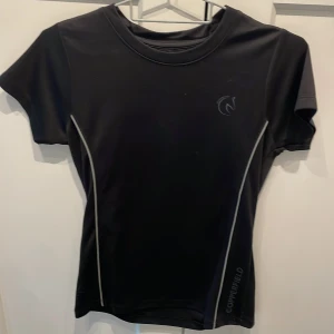 Svart tränings-tshirt Copperfield - Svart sportig t-shirt från Copperfield med korta ärmar och rund hals. Snygga grå linjer längs sidorna ger en cool look. Tillverkad i ett syntetmaterial som andas, perfekt för träning eller aktiva dagar. Diskret logga på bröstet och smal passform.