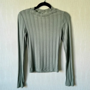 Ribbad grön långärmad tröja Gina Tricot - Snygg ribbad långärmad tröja från Gina Tricot i en ljusgrön nyans. Tröjan har en rund halsringning och smal passform som sitter tajt mot kroppen. Perfekt att styla med jeans eller kjol för en clean look.