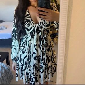 Plisserad kortklänning med svartvitt mönster - Supersnygg plisserad kortklänning med djup v-ringning och långa puffärmar från H&M i storlek S. Aldrig använd endast testad en gång!💘💘💘