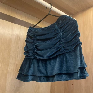 Söt Blå sammetskjol - Supersnygg blå sammetskjol, köpt i usa, i kort modell. Kjolen har volangkant och rynkade detaljer framtill som ger en cool och trendig look. Perfekt för dig som vill sticka ut lite extra med en mjuk och glansig känsla. Så skön. Passar xs,s och m då den är stretchig och lite stor i storleken. 