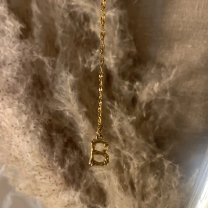 Guldigt halsband med bokstav B - Snyggt halsband i guldton med en kedja och ett hänge i form av bokstaven B. Hänget har en lite organisk, ojämn form som ger en cool och unik vibe. Perfekt accessoar för dig som vill ha något personligt och trendigt.