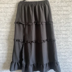 Svart långkjol med volanger - Säljer en svart långkjol med flera lager volanger och resår i midjan. Kjolen har en lätt skrynklig struktur och en slits framtill som ger extra rörelse. Perfekt för dig som gillar en bohemisk och avslappnad stil. Slits i fram, jag är 170cm och när jag har den lågmidjat så går den ända ner till fötterna. Helt ny och oanvänd, köpt utomlands. Storlek xs-m pga resår i midjan. 