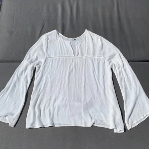 Vit blus med vida ärmar - Säljer en luftig vit blus med långa, vida ärmar och lätt v-ringning. Blusen har en avslappnad passform och är tillverkad i ett tunt, mjukt tyg som känns skönt mot huden. Perfekt för varmare dagar eller lager på lager. Stor i storleken.