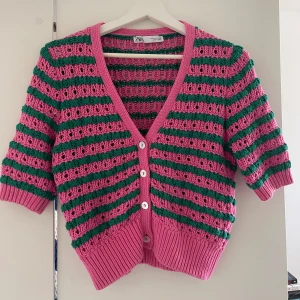 Rosa och grön randig kofta från Zara - Superfin kofta från Zara i rosa och grönt med randigt mönster. Koftan är stickad, har korta ärmar, v-ringning och knäpps med fyra vita knappar framtill. Croppad modell med bred ribbad mudd nedtill och vid ärmslut. Perfekt för vår och sommar!💕💕