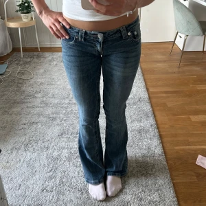 True Religion bootcut jeans blå - Säljer ett par klassiska blå jeans från True Religion med bootcut passform och låg midja. Jeansen har snygga detaljerade bakfickor med kontrastsömmar och silverfärgade knappar. Tillverkade i mjukt denimtyg som sitter riktigt bra.