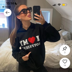 Svart hoodie med tryck 'I ❤️ MY BOYFRIEND' - Svart hoodie med vit och röd text på bröstet där det står 'I ❤️ MY BOYFRIEND'. Tröjan har huva och en avslappnad passform, perfekt för en chill och casual look. Klassisk känguruficka framtill och långa ärmar.