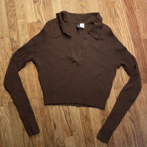 Brun ribbad tröja - Säljer en brun ribbstickad tröja från H&M Divided. Tröjan har en croppad passform, lång ärm och en snygg krage med v-ringad hals. Perfekt för lager-på-lager och passar till både jeans och kjol.🤎