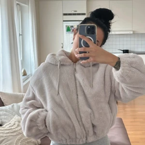 Ljusbeige teddyjacka med huva - Supermjuk och fluffig teddyjacka i ljusbeige med dragkedja framtill och huva med snörning. Jackan har en oversized passform och långa ärmar med resår vid ärmslut och midja. Perfekt för kalla dagar när du vill vara både varm och stylish.