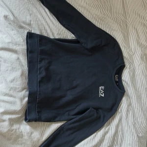 Mörkblå sweatshirt från EA7 Armani - Snygg mörkblå sweatshirt från EA7 Emporio Armani med rund halsringning och diskret logga på bröstet. Tröjan har långa ärmar och är tillverkad i mjuk bomull, perfekt för en clean och stilren look.