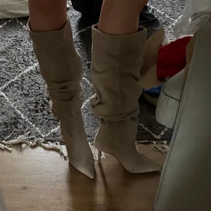 Beige mockastövlar med klack - Snygga beige stövlar i mocka med hög klack och spetsig tå. Bootsen är aldrig använda och lappen sitter kvar. 