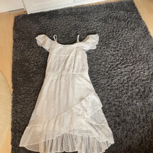 Vit prickig långklänning från Lindex - Supersöt vit långklänning från Lindex med små prickar, volangdetaljer och offshoulder-ärmar. Klänningen har ett lager med transparent tyg och en omlottvolang nedtill som ger extra flow. Perfekt för sommarens alla tillfällen!