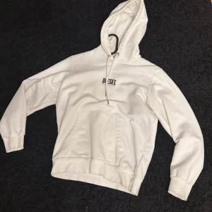 Vit hoodie från Diesel - Säljer en stilren vit hoodie från Diesel med logotyp på bröstet. Hoodien har en klassisk känguruficka och justerbar huva med snören. Perfekt för en avslappnad stil.