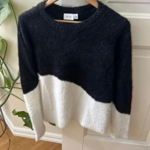 Svartvit stickad tröja från Vila - Mysig tröja från Vila i storlek S. Tröjan har en cool färgblock-design med svart upptill och vit nedtill. Den är långärmad och har en rund halsringning. Perfekt för dig som gillar en enkel men ändå trendig look.