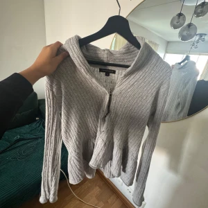 Grå ribbad kofta från Mywear Woman - Säljer en grå ribbad kofta från Mywear Woman i storlek M. Koftan har dragkedja framtill, lång ärm och en lite lösare passform. Perfekt för lager-på-lager och enkel att matcha med olika outfits.