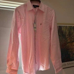Ralph Lauren Skjorta - L - Ralph Lauren skjorta, strl L – 798 kr  Helt ny rosa/vit randig skjorta från Ralph Lauren, storlek L - XL. Aldrig använd, tags kvar. Klassisk modell med broderad Polo-logga. Nypris ca 1 500 kr. Säljes för 800kr.  Skicka meddelande vid frågor!