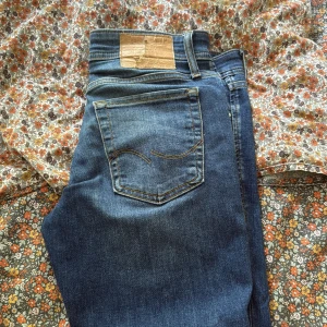 Blå jeans från Jack & Jones - Snygga blå jeans från Jack & Jones med klassisk femficksdesign och ljusa slitningar framtill. Jeansen har normal passform och är tillverkade i mjukt denimtyg med en skön känsla. Perfekta för dig som gillar en avslappnad och stilren look. Slim glen modellen 