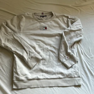 Vit sweatshirt från Tommy Hilfiger - Snygg vit sweatshirt från Tommy Hilfiger med broderad logga på bröstet och ärmslutet. Tröjan har rund halsringning, ribbade muddar och klassisk passform. Perfekt för dig som gillar stilren och enkel design med en touch av street. Och den har fickor på sidan av sweatshirten storlek 176cm nypris 629kr
