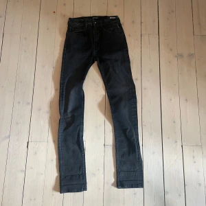 Svarta Replay jeans  - Snygga svarta jeans från Replay med klassisk femficksdesign och diskreta Replay-detaljer på bakfickan och insidan. Modellen har slim fit och raka ben, perfekt för dig som gillar en stilren look. Jeansen är tillverkade i mjukt denim-material.