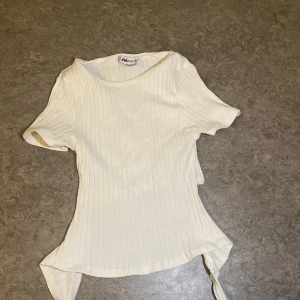 Vit ribbad topp med knyt från FB Sister - Superfin vit ribbad topp från FB Sister i storlek XS. Toppen har korta ärmar och snygga knytband i ryggen som ger en cool detalj. köpt på newyorker