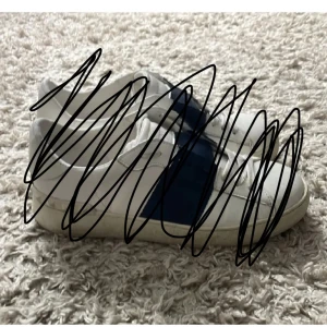 Vita sneakers med blå detalj - Snygga vita sneakers med en bred blå rand på sidan. Klassisk låg modell med snörning och rund tå. Perfekta för en clean och sportig look. Passar till det mesta och är lätta att matcha.