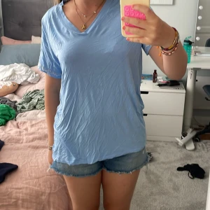 Ljusblå t-shirt från Change Lingerie - Säljer en ljusblå t-shirt från Change Lingerie i storlek M. Toppen har v-ringad hals och korta ärmar, med en loose passform som är chill och enkel att bära. Materialet känns mjukt och skönt mot huden, perfekt för varma dagar.