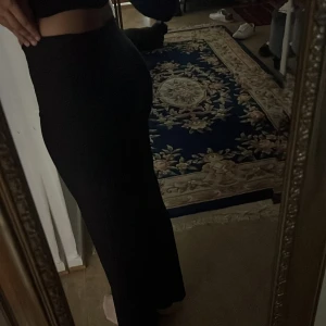 Svarta högmidjade wide byxor - Snygga svarta byxor med hög midja och wide passform. De har raka ben och sitter tajt över höften, vilket ger en clean och modern siluett. Perfekta att styla med crop tops eller hoodies för en trendig look.