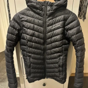 Svart dunjacka Peak Performance S - Säljer en svart dunjacka från Peak Performance i storlek S. Jackan har huva, dragkedja framtill och två fickor med dragkedja. Den är lätt och smidig, perfekt för kyliga dagar. Klassisk Peak Performance-logga på bröstet och ärmen. Enda negativa är att det är defekter på vänster arm men man tänker ej på det när man har på sig den❤️