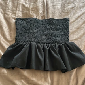 Svart bandeau tubtopp från SHEIN - Svart bandeau tubtopp från SHEIN i storlek XS. Toppen har smockad överdel och en bred volang nedtill som ger en snygg och trendig siluett. 