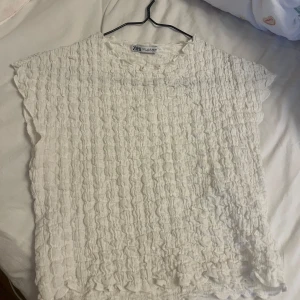 Vit strukturerad topp från Zara - Superfin vit topp från Zara med coolt strukturerat tyg och lös passform. Toppen är ärmlös och har en lätt rynkad effekt över hela ytan som ger en unik look. Perfekt att styla med jeans eller kjol för en fräsch vibe.
