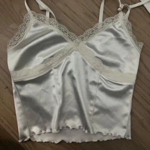 Satinlinnen med spetsdetaljer - Två stilrena linnen i satin, ett i vitt och ett i svart. Båda har tunna axelband, v-ringad hals och fina spetsdetaljer längs urringningen. Perfekta att styla med jeans eller kjol för en trendig look. Båda gäller för samma pris 