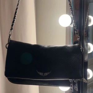 Svart axelväska med kedjerem - Snygg svart axelväska med silverfärgade detaljer och dragkedjor. Finns två stycken kedjor till väskan, en lite längre o en lite kortare❤️Använd max två gånger därav fint skick. Säljer pågrund av att jag inte använder den❤️