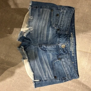 Blå low waist  jeansshorts från American Eagle - Snygga blå jeansshorts från American Eagle med fransiga kanter och klassisk femficksdesign. Shortsen har låg midja, slitna detaljer och är mycket populära.