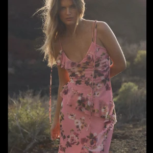 Rosa blommig linnetopp med volang - Supersöt rosa linnetopp från Zara med blommigt mönster, tunna axelband med knyt och asymmetrisk volangkant. Toppen har v-ringning och är perfekt för varma dagar när du vill sticka ut lite extra. Endast testad i butik och har tyvärr inte kommit till användning💞