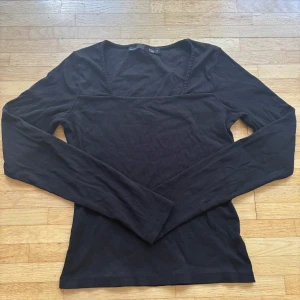 Svart ribbad långärmad topp från Lager 157 - Svart långärmad topp från Lager 157 i ribbad bomull. Modellen har en snygg fyrkantig halsringning och sitter tight mot kroppen. Perfekt att styla med jeans eller kjol för en clean och enkel look.