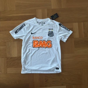 Vit Santos FC fotbollströja  - Tja, säljer nu min vit fotbollströja från Santos FC. Tröjan är helt oanvänd med lappen kvar. Det är i storlek M och vid frågor och funderingar är det bara att höra av sig!