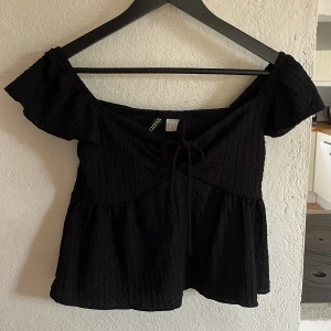 Svart blus med knytbar framdel  - Supersöt svart blus, den är lite off shoulder med knyt fram. Materialet är lite krinklat. Suuuuper fin att ha på sommaren 🫶🏼