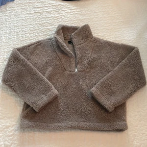 Beige fleece-tröja från BikBok - Mysig beige fleece-tröja från BikBok i storlek M. Tröjan har en hög krage och half zip-dragkedja framtill. Materialet är fluffigt och tillverkat av återvunnen polyester, perfekt för kalla dagar. Långärmad och loose fit för extra comfort. Perfekt till hösten.