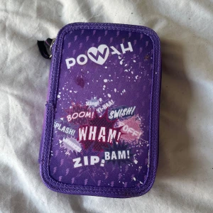 Lila pennfodral - Söt lila pennfodral med POWAH-tryck och coola serietidningsord som WHAM, BOOM och ZIP! Fodralet har dragkedja runt om och elastiska band för pennor på insidan. Perfekt för att hålla koll på alla dina pennor och sudd i skolan tex. Den kommer inte mer till användning. Kontakta gärna innan köp!