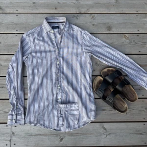 Randig skjorta från Massimo Dutti - Snygg skjorta från Massimo Dutti i storlek S, grå/beige och vitt färg med vertikala ränder. Nypris ligger på 900kr. Skjortan har klassisk krage, knäppning framtill och lång ärm. Tillverkad i 100% bomull, perfekt för en chill och stilren look. Broderad logga på ger extra detalj.